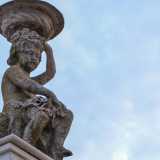 Pi� in alto una cornice a dentelli, che corre lungo tutto l�edificio, cinge un terrazzino abbellito da due statue di bambini che reggono un vaso sul capo